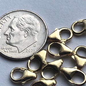 May include: A group of eight gold-toned lobster clasps, each with a small 'GF' marking. The clasps are scattered on a white surface, with a US dime for scale.