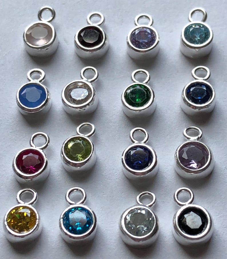 May include: Assortment of 16 silver charm pendants with different colored gemstones. Each pendant features a round gemstone in a silver setting with a loop for attaching to a chain or bracelet.