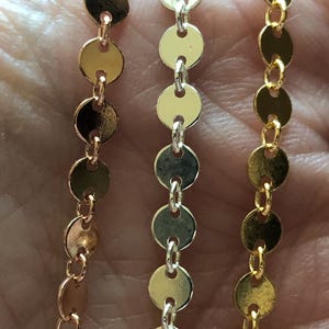 Op de afbeelding: Drie strengen ketting met ronde, platte, metalen schakels. De kettingen zijn goud, zilver en roségoud.
