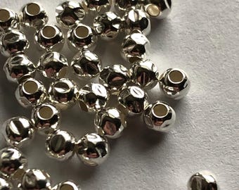 Op de afbeelding: Een stapel zilverkleurige metalen kralen met een getextureerd oppervlak. De kralen zijn rond en hebben een gat in het midden.
