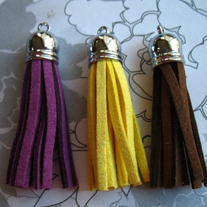 May include: Three suede tassels with silver metal tops. The tassels are purple, yellow, and brown.