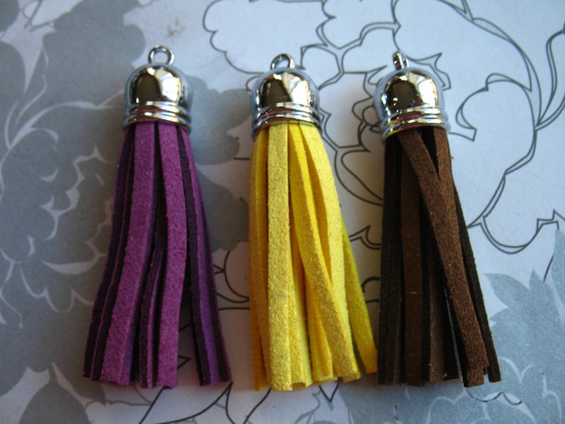May include: Three suede tassels with silver metal tops. The tassels are purple, yellow, and brown.