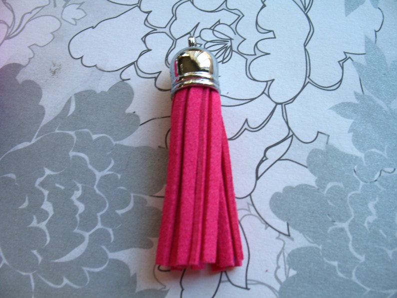May include: A bright pink tassel with a silver metal top. The tassel is made of soft, fuzzy material.