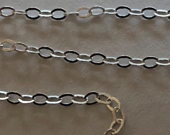Puede incluir: Un collar de cadena de plata con eslabones ovalados. La cadena está sobre una superficie blanca.