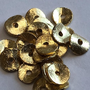 Peut inclure: Un tas de perles en métal de couleur dorée avec une surface texturée et un trou au centre. Les perles sont rondes et plates.