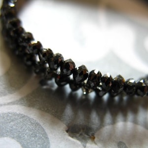 May include: A black diamond bracelet made of small, faceted black diamonds. The bracelet is made of a thin, flexible chain.