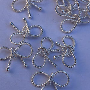 May include: A group of silver metal bow charms with a twisted rope design. The charms are small and delicate, and they would be perfect for adding a touch of elegance to jewelry or crafts.