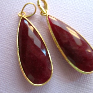 May include: A pair of gold-toned earrings with teardrop-shaped red gemstone pendants.