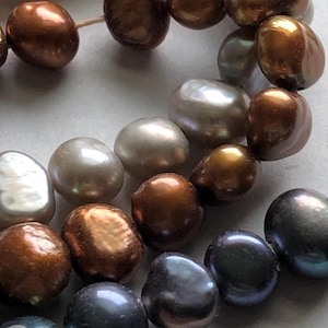 May include: A strand of pearls with a variety of colors, including white, brown, black, and iridescent. The pearls are all different shapes and sizes, and they are strung together on a clear thread.