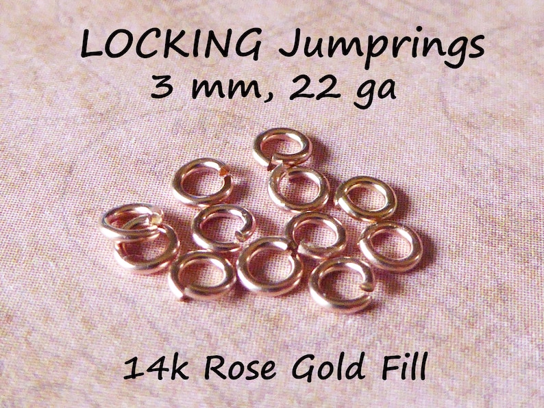 May include: A close-up of 14k rose gold filled locking jump rings. The jump rings are 3 mm in diameter and 22 gauge. The jump rings are scattered on a pink fabric surface.