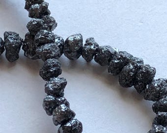 May include: A strand of black diamond beads, each bead is irregularly shaped and has a rough, natural texture.