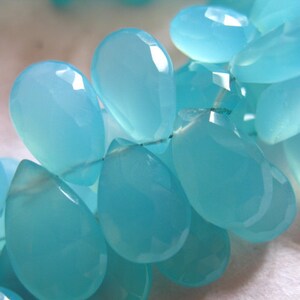 Puede incluir: Una hebra de cuentas de piedras preciosas de color azul claro, cada cuenta tiene forma de l&aacute;grima con un acabado liso y pulido.
