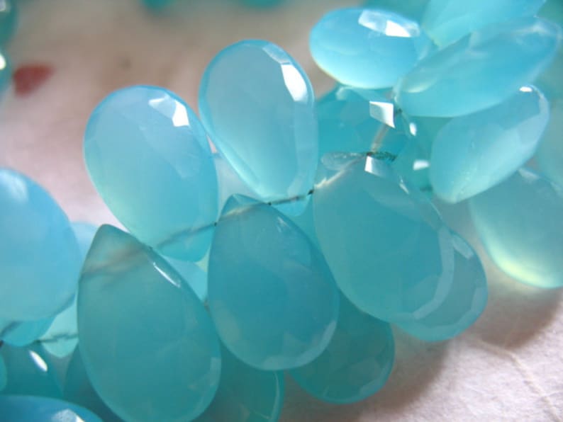 Puede incluir: Una hebra de cuentas de piedras preciosas de color azul claro, cada cuenta tiene forma de l&aacute;grima con un acabado liso y pulido.