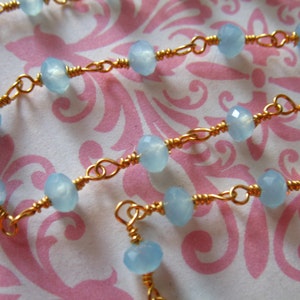 May include: A delicate gold chain necklace with light blue gemstone beads. The necklace is made with small, round beads and is strung on a thin gold chain.