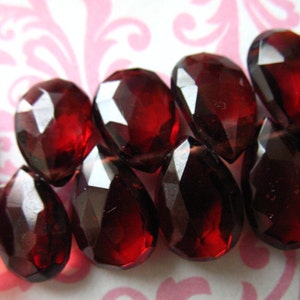 May include: A strand of deep red faceted glass beads in a teardrop shape.