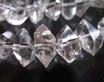 Op de afbeelding: Een close-up van een streng heldere kwartskristallen, elk met een gefacetteerde, diamantvormige vorm. De kristallen zijn in een rij gerangschikt, met hun punten naar de kijker gericht.