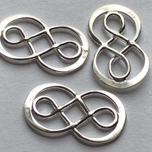 May include: Three silver infinity symbol charms with a 925 stamp on one of the charms.