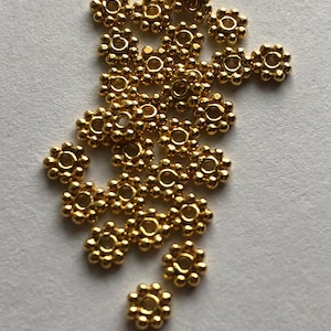 May include: A pile of gold-colored metal beads with a flower-like design. Each bead has a small hole in the center.