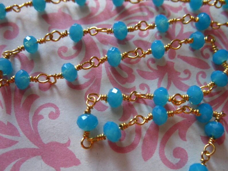 May include: A gold chain necklace with light blue gemstone beads. The chain is made of small, linked gold wire.