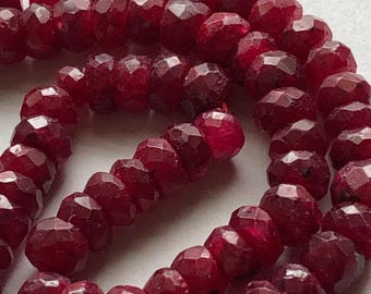 May include: A strand of deep red ruby beads, each bead is faceted and has a slightly irregular shape. The beads are strung on a thin red thread.