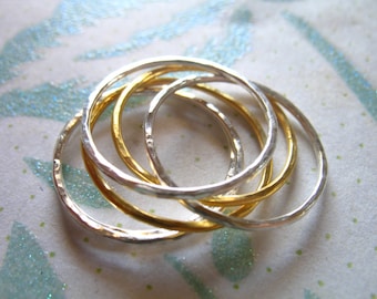 Peut inclure: Un ensemble de quatre bagues simples et minimalistes, deux en argent et deux en or, empilées et entrelacées. Les bagues sont lisses et ont une texture légèrement martelée.