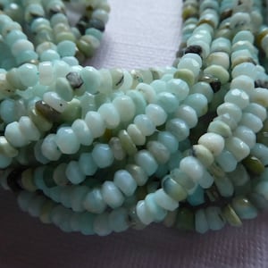 May include: A strand of light blue and green gemstone beads. The beads are faceted and have a slightly irregular shape. The beads are strung on a clear thread.