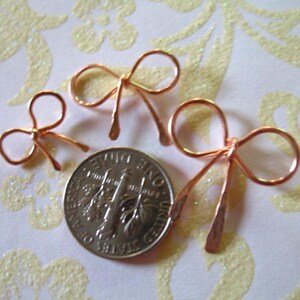 May include: Three copper wire bows of varying sizes. The bows are arranged in a row from largest to smallest. The largest bow is about the size of a US quarter.