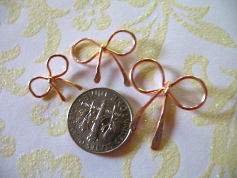 May include: Three copper wire bows of varying sizes. The bows are arranged in a row from largest to smallest. The largest bow is about the size of a US quarter.