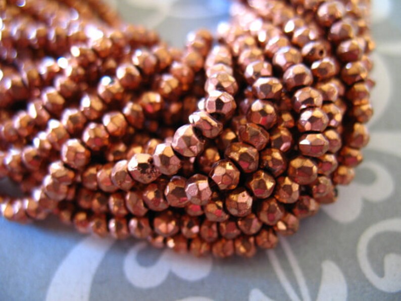 May include: A strand of copper-colored faceted beads. The beads are small and have a metallic sheen.