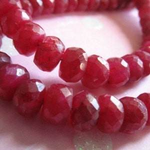 Puede incluir: Una hebra de cuentas de rub&iacute; rojo intenso, facetadas y pulidas, ensartadas para formar un collar o pulsera. Las cuentas est&aacute;n dispuestas en primer plano, mostrando su rico color y sus intrincadas facetas.