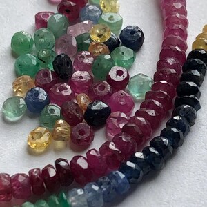 May include: A strand of gemstone beads in shades of red, blue, green, and yellow. The beads are faceted and have a polished finish.