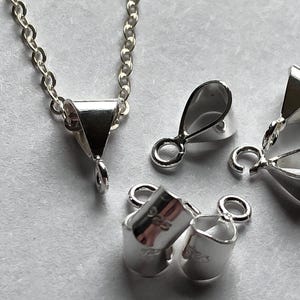 Puede incluir: Un juego de cierres de joyería plateados. Los cierres son de varias formas, incluyendo una lágrima, un triángulo y un rectángulo. Los cierres son todos de metal y tienen un acabado brillante.