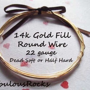 May include: A close-up of a gold-filled round wire, 22 gauge, in dead soft or half hard. The wire is wrapped around a brown ribbon and is on a white background with red hearts.