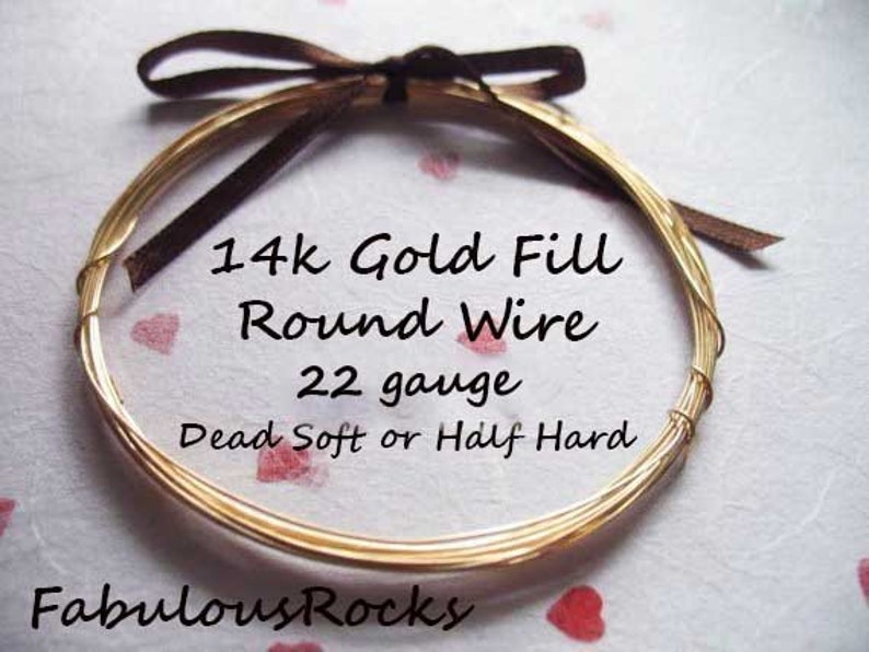 May include: A close-up of a gold-filled round wire, 22 gauge, in dead soft or half hard. The wire is wrapped around a brown ribbon and is on a white background with red hearts.