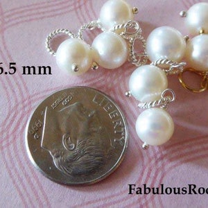 May include: A close-up of a group of white pearl beads with silver and gold accents. The pearls are 6.5 mm in diameter and are arranged in a cluster. The beads are on a pink surface with a silver coin in the background.