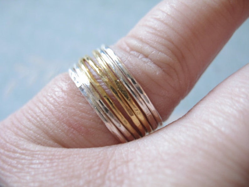 May include: A stack of thin gold and silver rings worn on a finger.