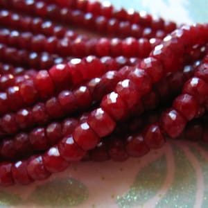 May include: A strand of deep red faceted gemstone beads. The beads are small and round, and they are strung together on a clear thread.