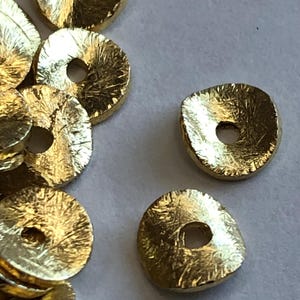 May include: A pile of gold-coloured metal beads with a textured surface and a hole in the centre. The beads are round and flat.