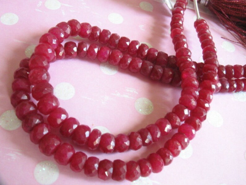 Puede incluir: Una hebra de cuentas de piedras preciosas facetadas de color rojo intenso. Las cuentas est&aacute;n enhebradas en un hilo transparente y est&aacute;n dispuestas en un patr&oacute;n circular.