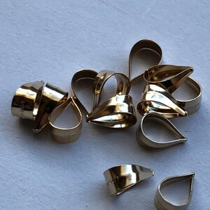 Puede incluir: Un grupo de diez baúles de colgantes de metal de color dorado. Los baúles tienen forma de lágrima y un acabado liso y brillante.