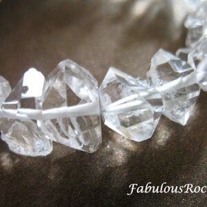 May include: A bracelet made of clear quartz crystals, each crystal is faceted and has a geometric shape. The bracelet is made of many crystals that are strung together.