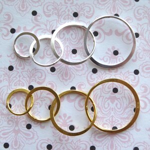 May include: A set of five interlocking rings, three silver and two gold, arranged in a circle. The rings are of varying sizes and are on a white background with a pink floral pattern.