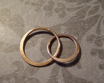 May include: Two interlocking gold rings, one slightly larger than the other, on a textured gray surface.
