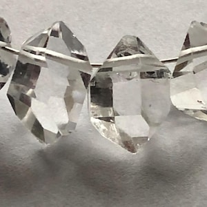 Puede incluir: Una hebra de cuentas de cristal de cuarzo transparente, cada cuenta está facetada y tiene una forma puntiaguda. Las cuentas están enhebradas en un alambre de plata.