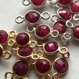 Op de afbeelding: Een close-up van een groep robijnrode edelsteenverbinders met gouden en zilveren springringen. De connectoren zijn perfect voor het maken van sieraden.
