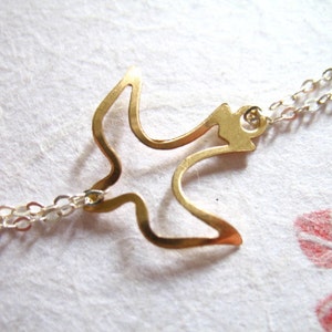 Puede incluir: Un collar dorado con una cadena delicada y un colgante de p&aacute;jaro simple y calado.