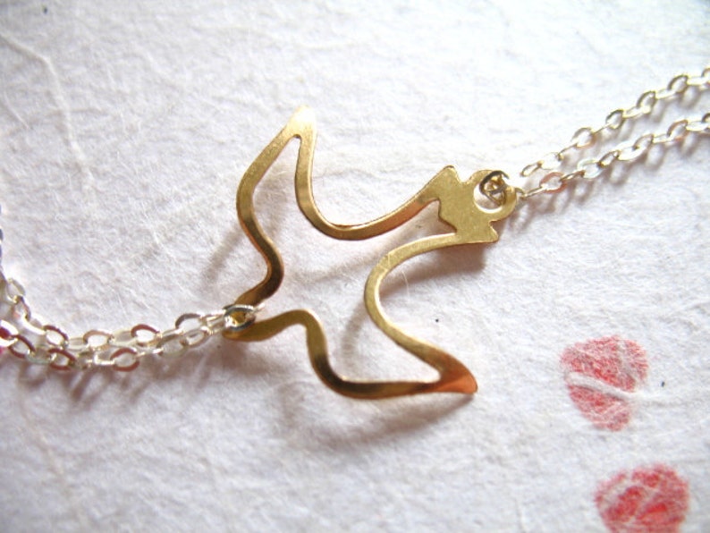 Puede incluir: Un collar dorado con una cadena delicada y un colgante de p&aacute;jaro simple y calado.