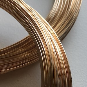 May include: Close-up of a spool of gold-colored wire. The wire is wound tightly together, creating a smooth, shiny surface.