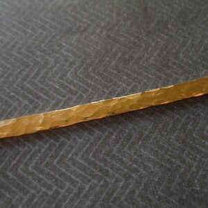 May include: A gold-colored metal bar with a hammered texture and two holes at each end. The bar is about 5 inches long.
