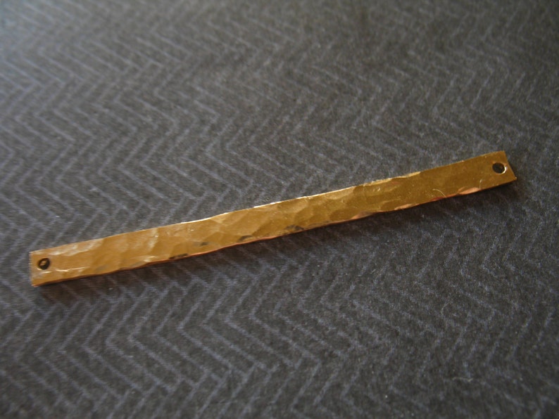 May include: A gold-colored metal bar with a hammered texture and two holes at each end. The bar is about 5 inches long.